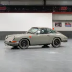 Seitenansicht eines Porsche 912 Coupé von 1966 in Zeltgrau mit schwarzen Felgen, fotografiert in einer modernen Halle.