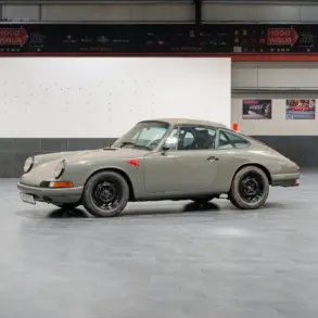 Seitenansicht eines Porsche 912 Coupé von 1966 in Zeltgrau mit schwarzen Felgen, fotografiert in einer modernen Halle.