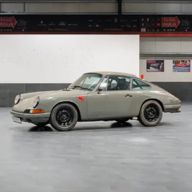 Seitenansicht eines Porsche 912 Coupé von 1966 in Zeltgrau mit schwarzen Felgen, fotografiert in einer modernen Halle.