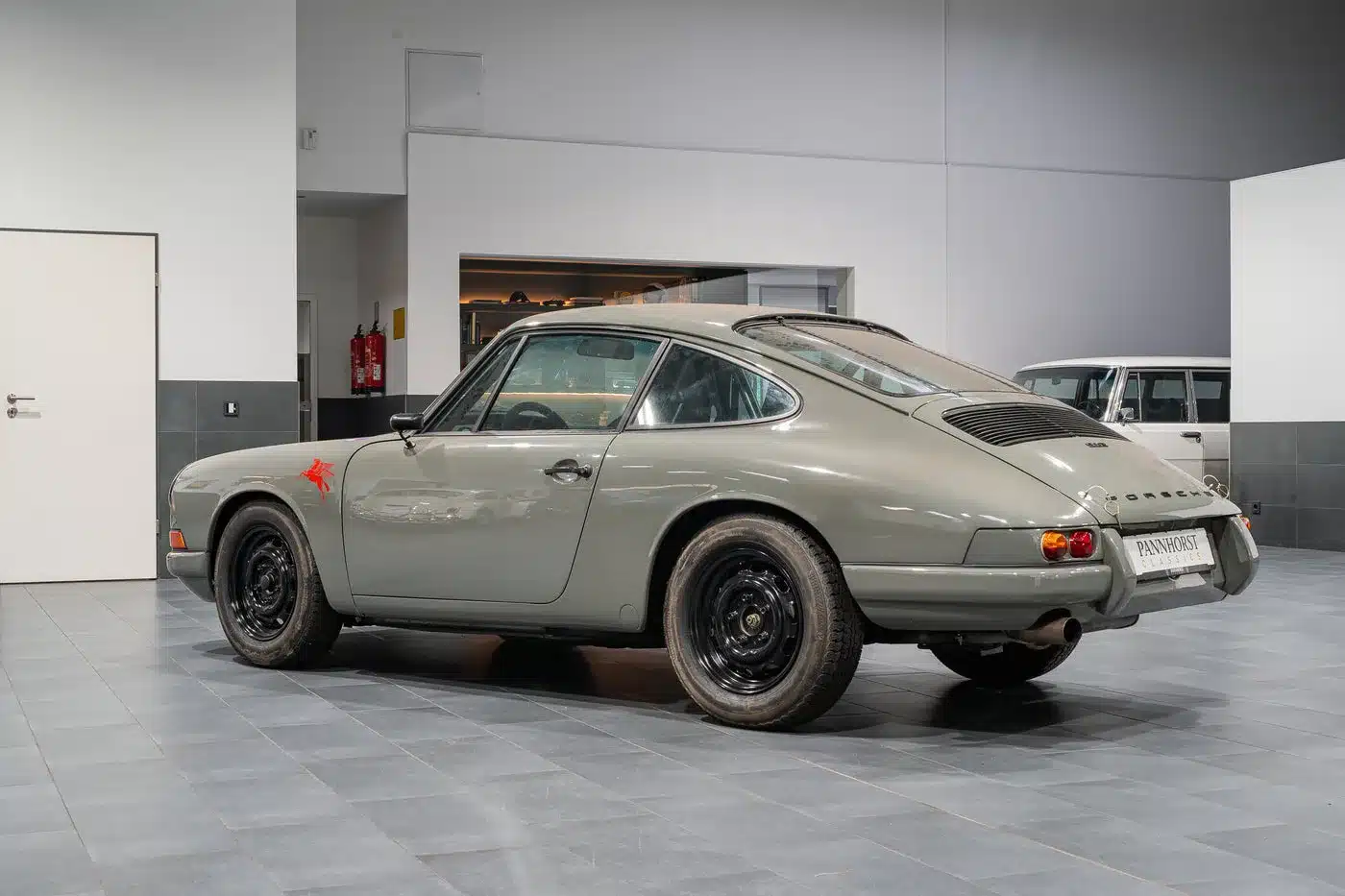 Seitenansicht eines Porsche 912 Coupé von 1966 in Zeltgrau, rennsportlich umgebaut, auf schwarzen Stahlfelgen, ausgestellt in einer Halle.