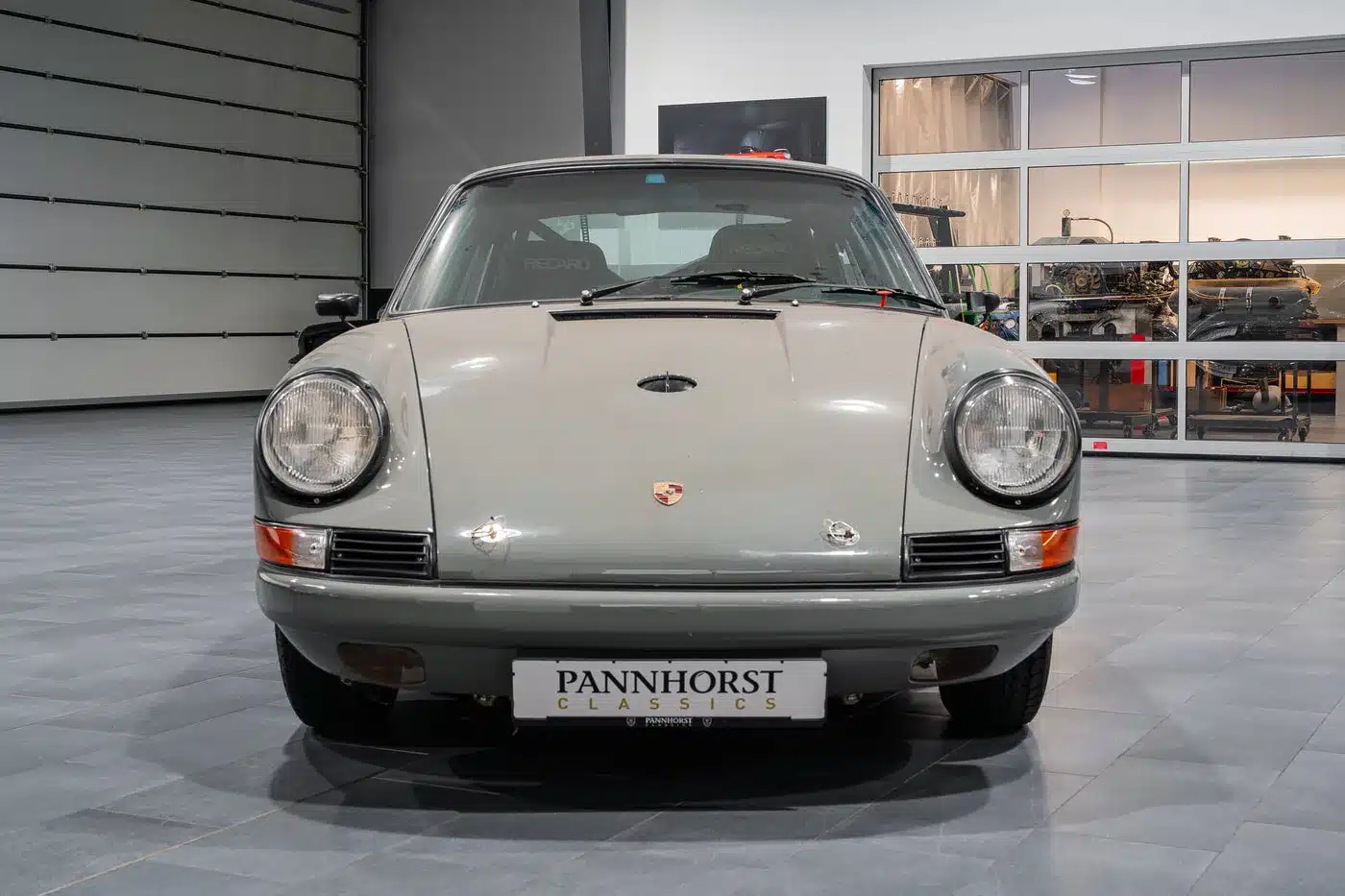 Porsche 912 Coupé von 1966 in Zeltgrau, rennsportlich umgebaut, frontal in einer modernen Werkstatthalle.