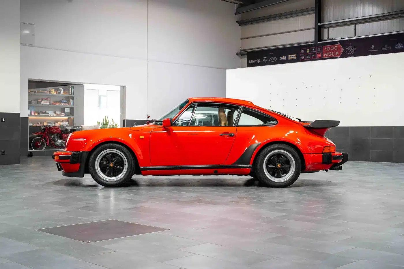 Seitenansicht eines roten Porsche 930 Turbo in einer modernen Ausstellungshalle.