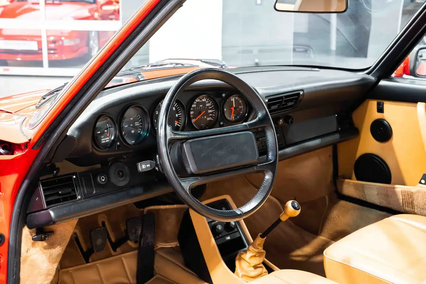 Innenraum und Cockpit eines Porsche 930 Turbo mit schwarzem Lenkrad, Armaturenbrett und beigem Interieur.