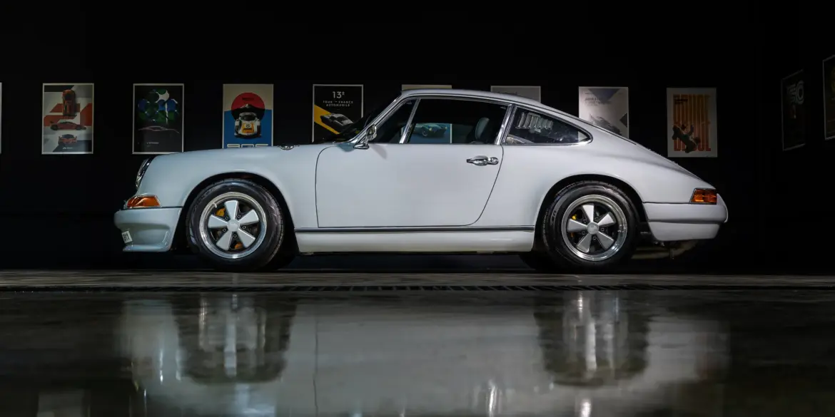 Weißer Porsche 964 C2 Backdate von der Seite vor dunklem Hintergrund mit beleuchteten Postern.