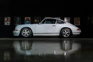 Weißer Porsche 964 C2 Backdate von der Seite vor dunklem Hintergrund mit beleuchteten Postern.