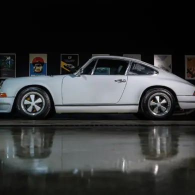 Weißer Porsche 964 C2 Backdate von der Seite vor dunklem Hintergrund mit beleuchteten Postern.
