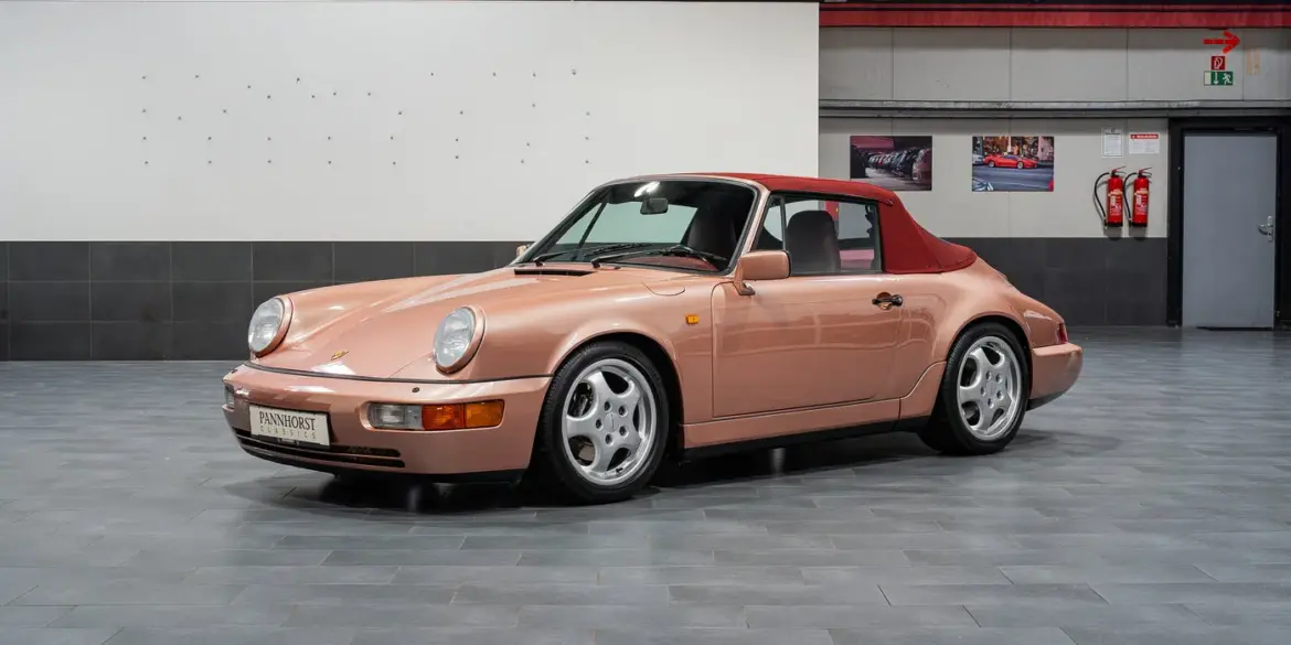 Porsche 964 Carrera 4 Cabriolet in roségold mit rotem Verdeck, seitlich fotografiert, in einer modernen Ausstellungshalle