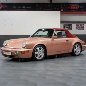 Porsche 964 Carrera 4 Cabriolet in roségold mit rotem Verdeck, seitlich fotografiert, in einer modernen Ausstellungshalle