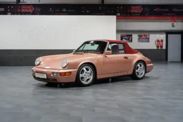 Porsche 964 Carrera 4 Cabriolet in roségold mit rotem Verdeck, seitlich fotografiert, in einer modernen Ausstellungshalle