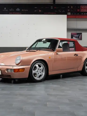 Porsche 964 Carrera 4 Cabriolet in roségold mit rotem Verdeck, seitlich fotografiert, in einer modernen Ausstellungshalle