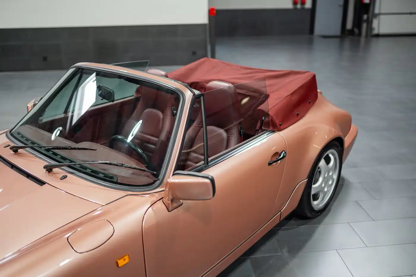 Detailansicht eines Porsche 964 Carrera 4 Cabriolets in rosé mit bordeauxrotem Verdeck und Interieur, fotografiert in einer Halle.