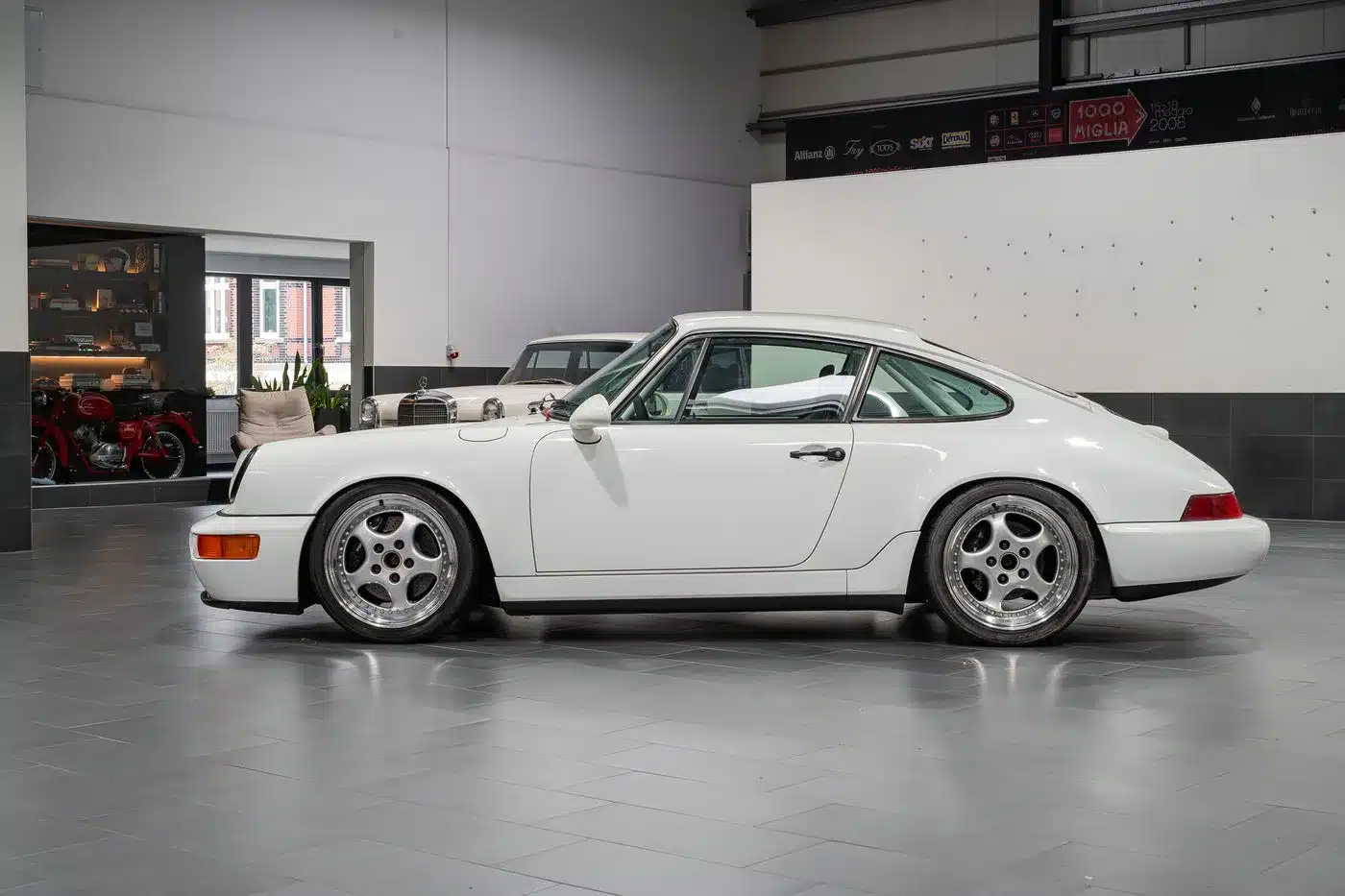 Weißer Porsche 964 Carrera Cup von 1993 in einer modernen Fahrzeughalle seitlich fotografiert
