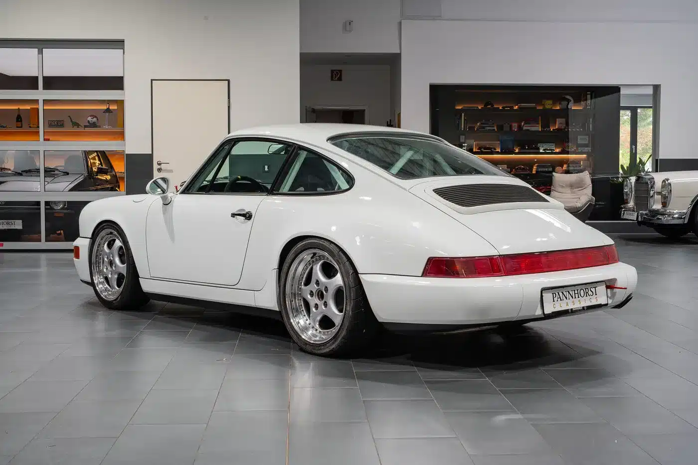 Weißer Porsche 964 Carrera Cup von 1993, seitlich von hinten in einer modernen Garage fotografiert.
