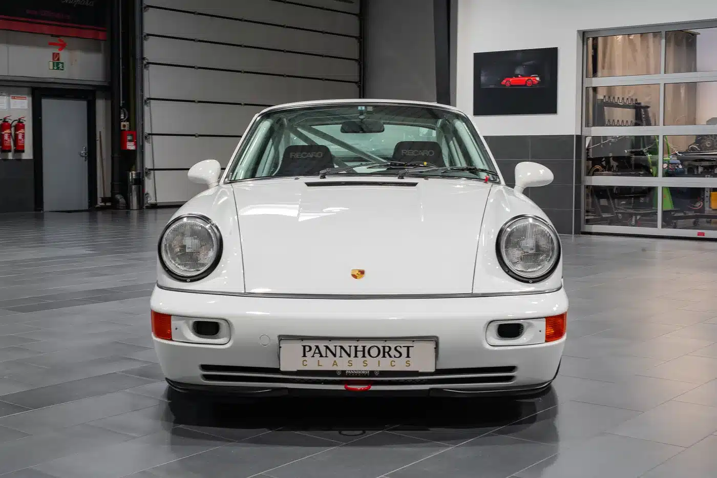 Frontansicht eines weißen Porsche 964 Carrera Cup von 1993 in einer modernen Werkstatthalle