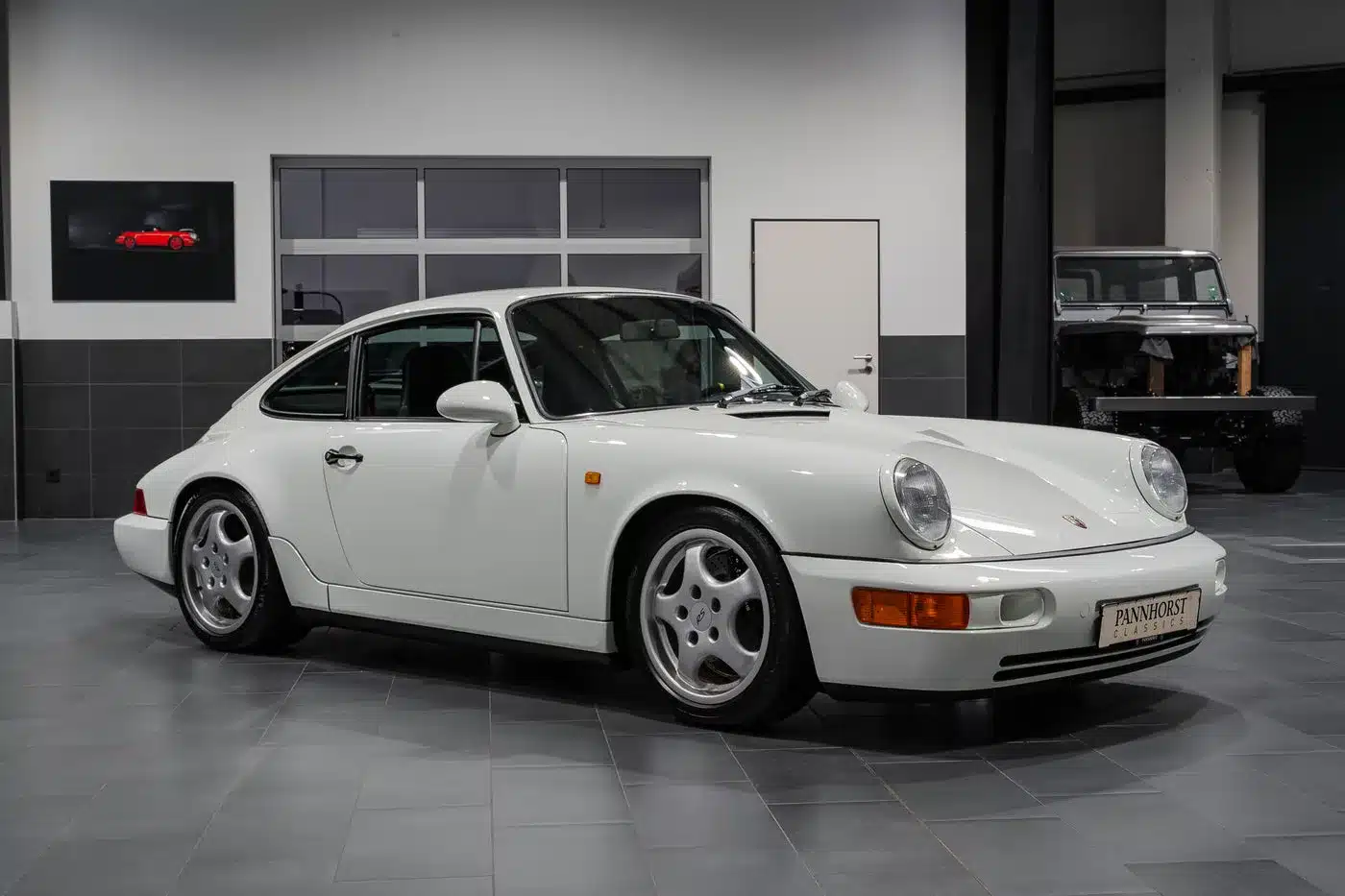 Weißer Porsche 964 RS steht in einem modernen Showroom auf grauen Fliesen.
