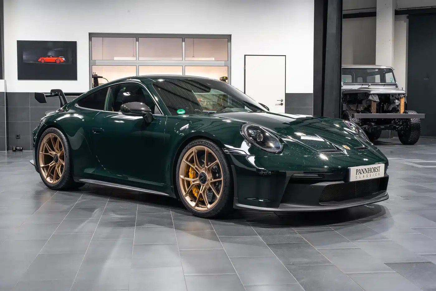 Grüner Porsche 992.1 GT3 mit goldenen Felgen in einer modernen Ausstellungshalle