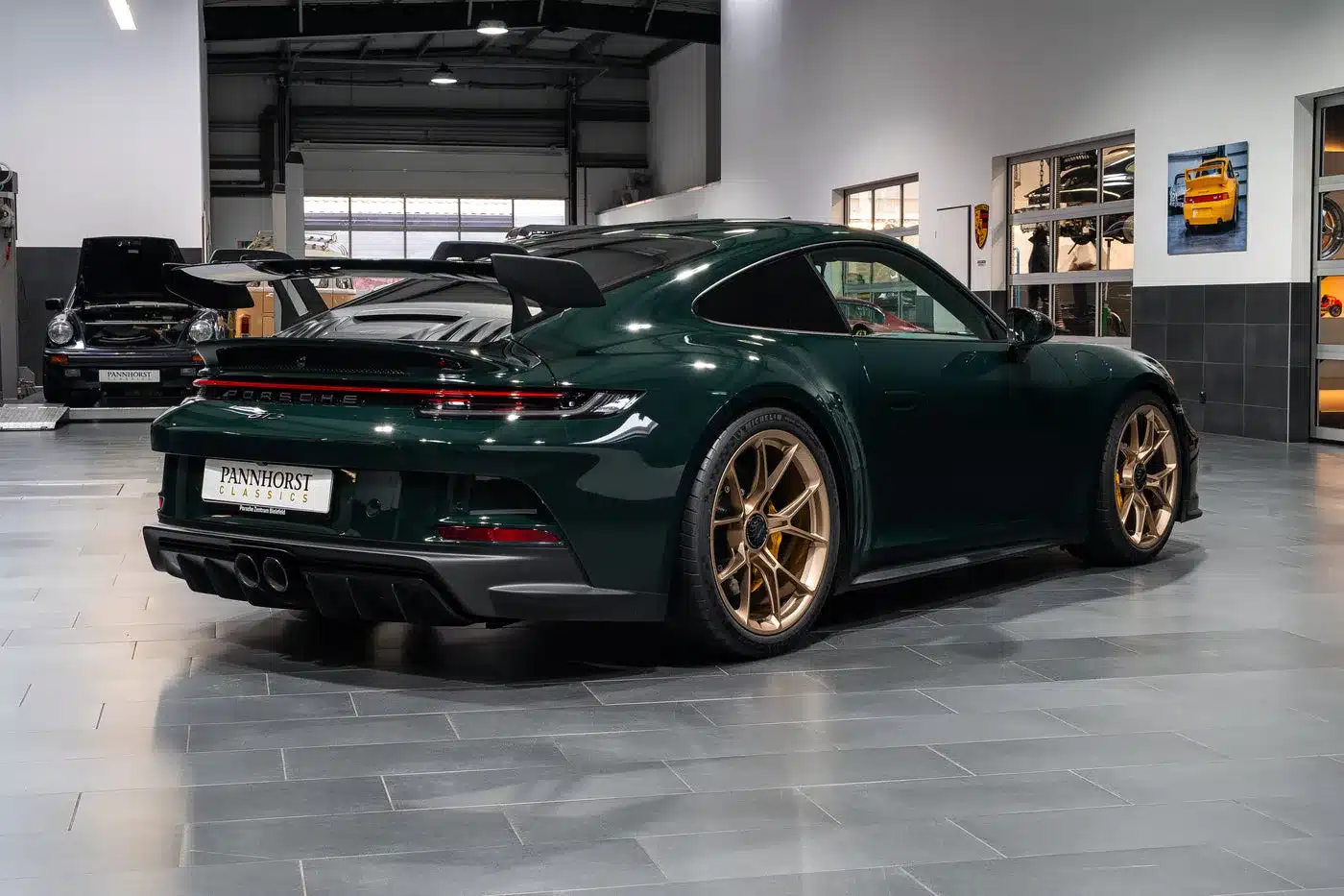Heckansicht eines dunkelgrünen Porsche 992.1 GT3 mit goldenen Felgen im Autohaus