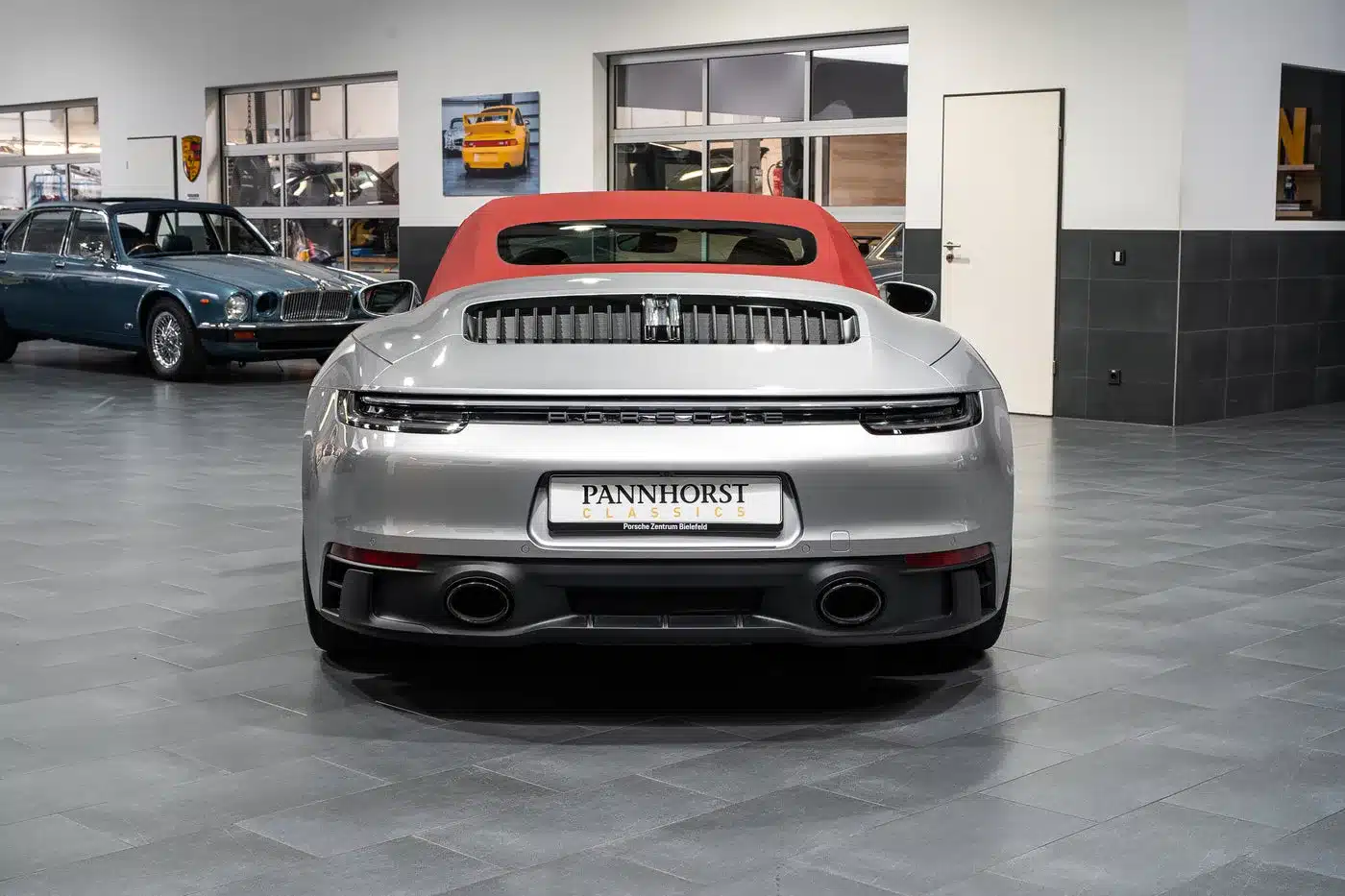 Heckansicht eines silbernen Porsche 992 911 Carrera GTS Cabriolet mit rotem Stoffverdeck im Ausstellungsraum