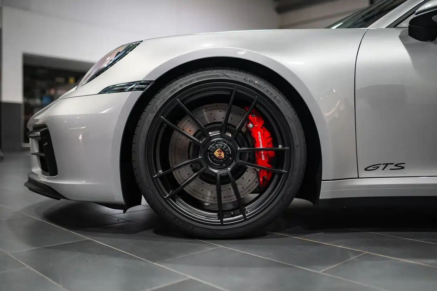 Nahaufnahme der Vorderachse eines silbernen Porsche 911 Carrera GTS Cabriolet mit schwarzer Sportfelge und rotem Bremssattel