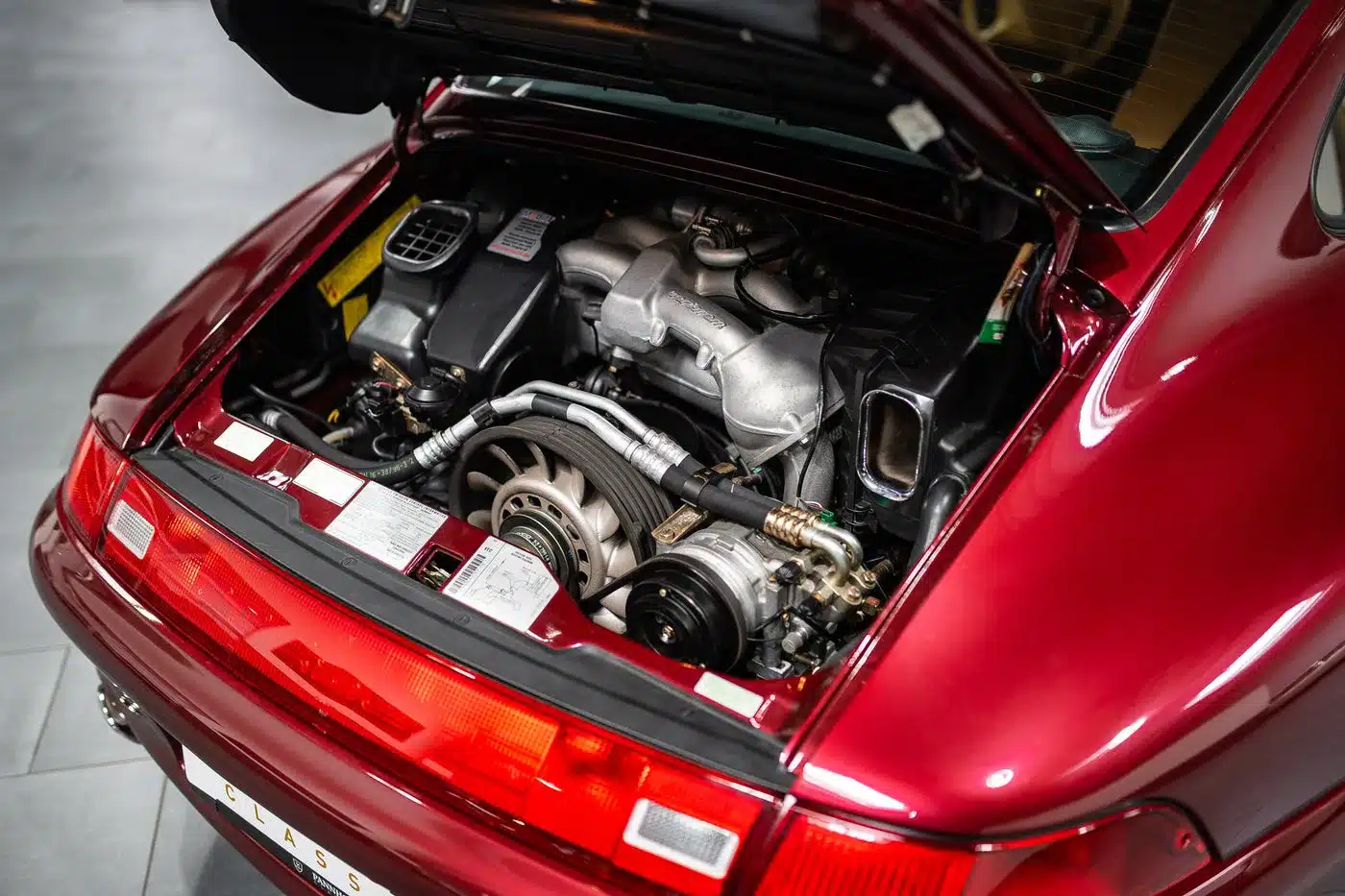 Offener Motorraum eines Porsche 993 Carrera 4S mit sichtbar luftgekühltem Boxermotor in Arena Red Metallic.