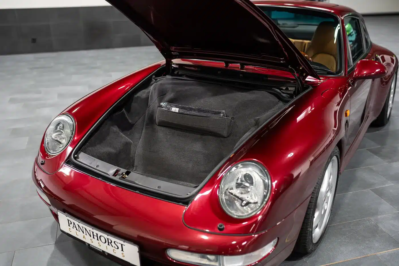 Frontalansicht auf den offenen Kofferraum (Frunk) eines Porsche 993 Carrera 4S in Arena Rot Metallic mit beigem Interieur.