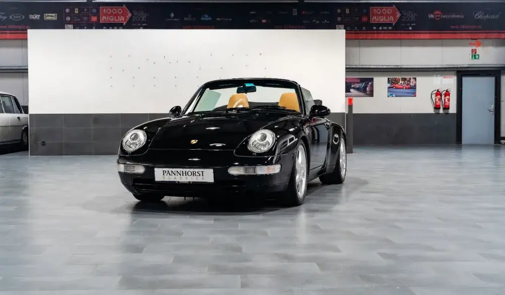 Frontansicht eines schwarzen Porsche 993 Carrera Cabriolet mit beigem Innenraum, ausgestellt in einer Halle