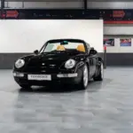 Frontansicht eines schwarzen Porsche 993 Carrera Cabriolet mit beigem Innenraum, ausgestellt in einer Halle