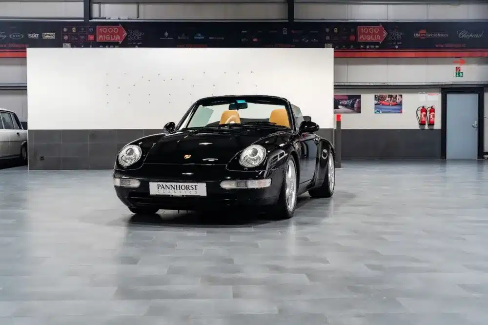Frontansicht eines schwarzen Porsche 993 Carrera Cabriolet mit beigem Innenraum, ausgestellt in einer Halle