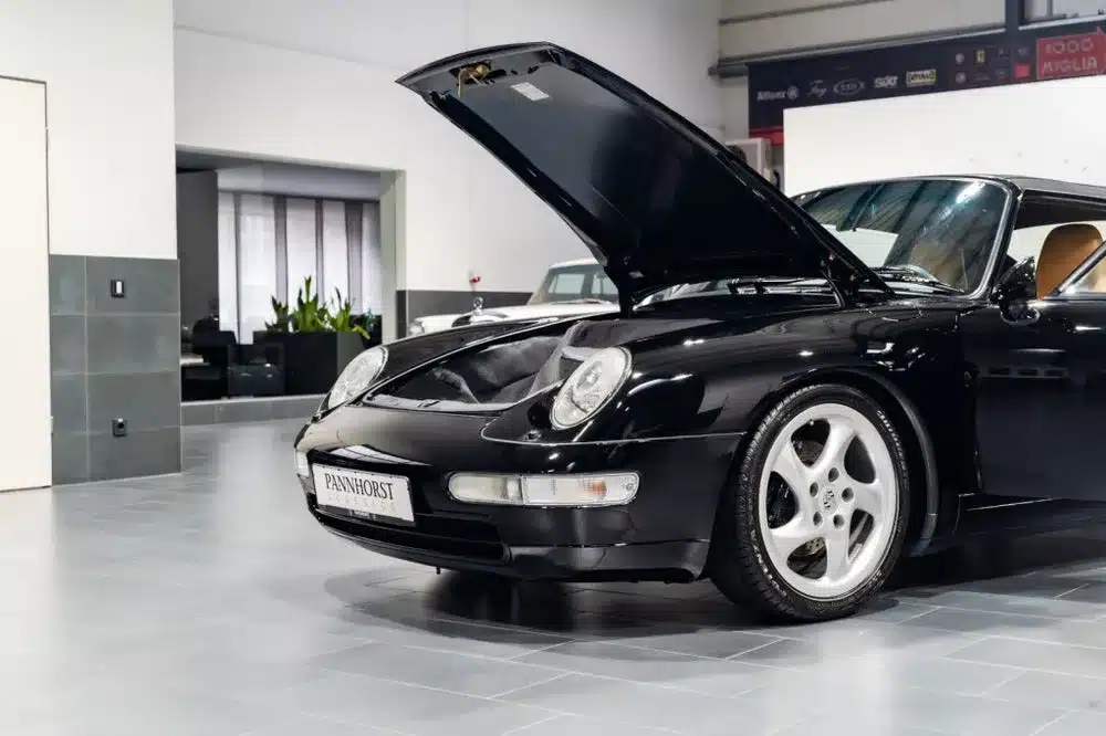 Schwarzes Porsche 993 Carrera Cabriolet, Baujahr 1996, mit geöffnetem Kofferraumdeckel im Innenraum einer Werkstatt.