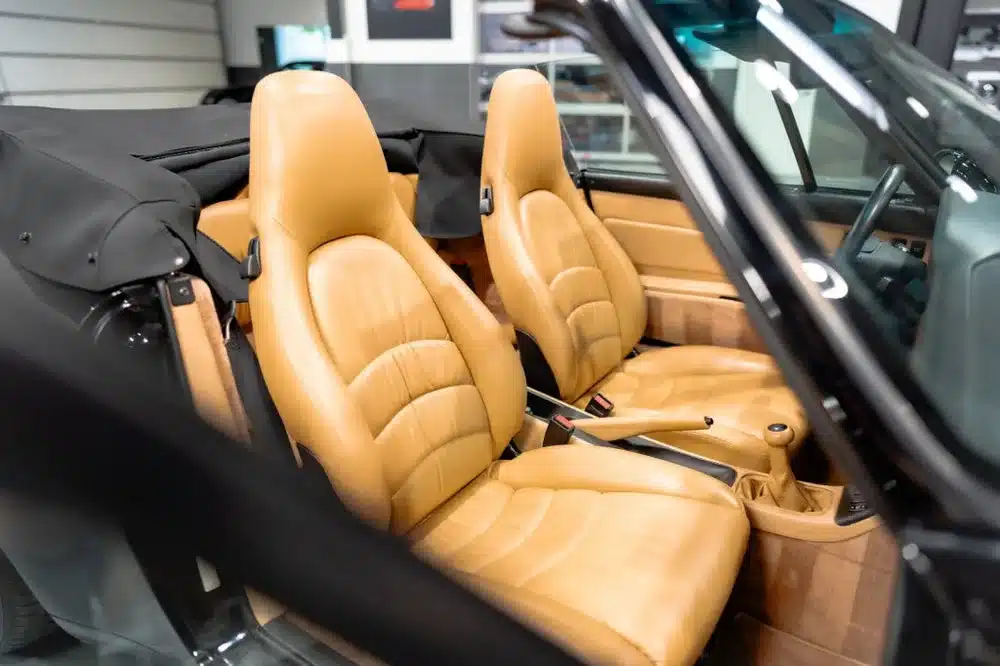 Innenraum eines Porsche 993 Carrera Cabriolet mit beigen Ledersitzen und offenem Verdeck.