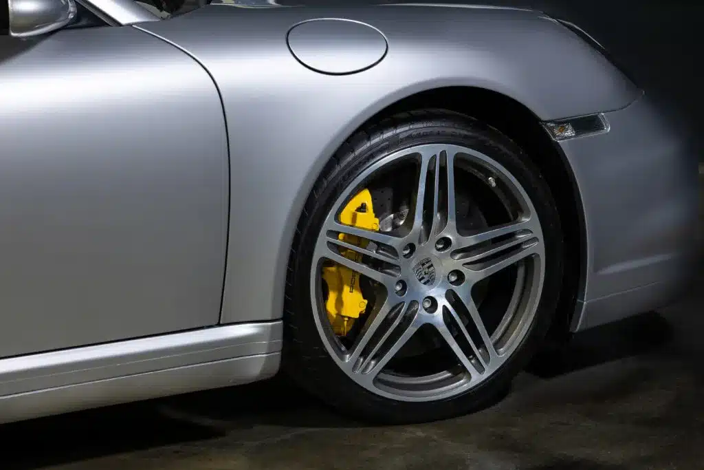 Detailaufnahme der Frontfelge und der gelben Carbon-Keramik-Bremsen eines silbernen Porsche 997 Turbo 2006