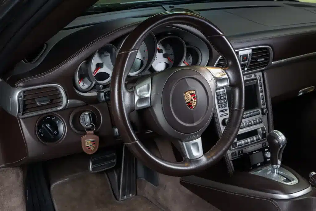 Detailaufnahme des Innenraums und Armaturenbretts eines Porsche 997 Turbo (Baujahr 2006) mit braunem Leder und Sportlenkrad.