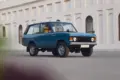 Restaurierter Range Rover Classic in Tuscan Blue, Baujahr 1975, steht auf einer Straße vor einem hellen Gebäude mit Rundbogenfenstern