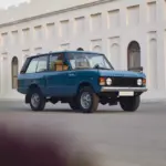 Restaurierter Range Rover Classic in Tuscan Blue, Baujahr 1975, steht auf einer Straße vor einem hellen Gebäude mit Rundbogenfenstern
