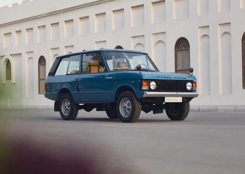 Restaurierter Range Rover Classic in Tuscan Blue, Baujahr 1975, steht auf einer Straße vor einem hellen Gebäude mit Rundbogenfenstern