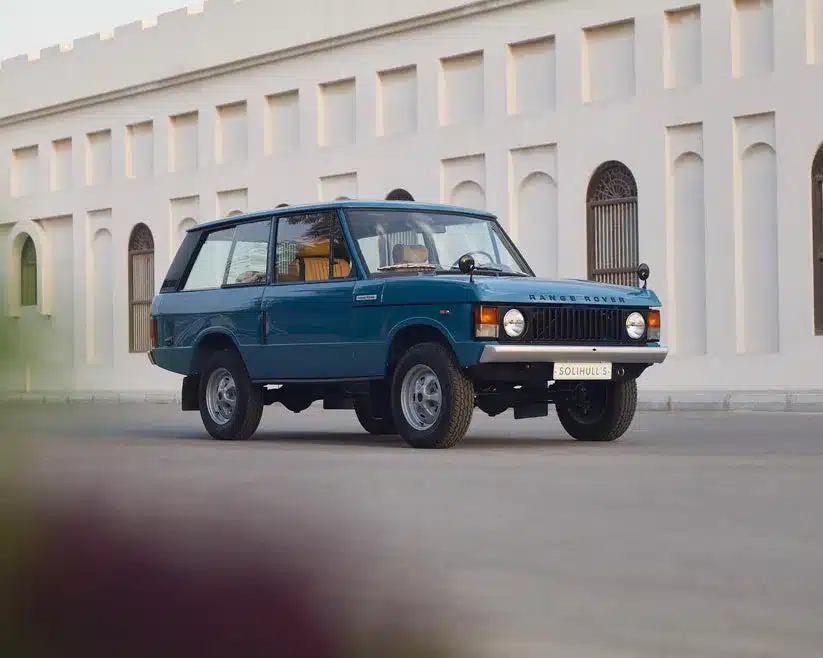 Restaurierter Range Rover Classic in Tuscan Blue, Baujahr 1975, steht auf einer Straße vor einem hellen Gebäude mit Rundbogenfenstern
