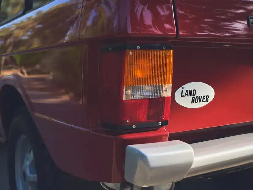 Detailaufnahme des Hecks eines Range Rover Classic 1976 in Masai Red mit Land Rover-Aufkleber und originaler Rückleuchte.