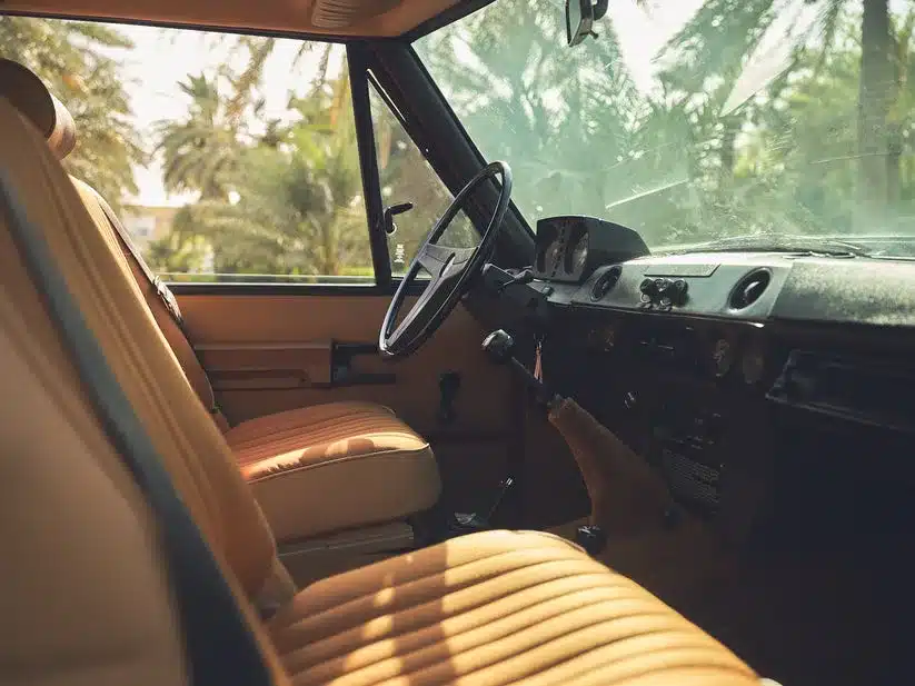 Sicht auf den Innenraum eines restaurierten Range Rover Classic von 1976, beiger Sitz und Armaturenbrett im Sonnenschein