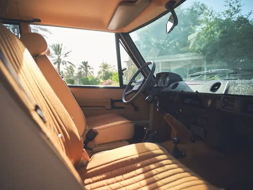 Klassischer Innenraum eines Range Rover Classic von 1981 mit beigen Sitzen und Lenkrad, Licht fällt durch die Fenster.
