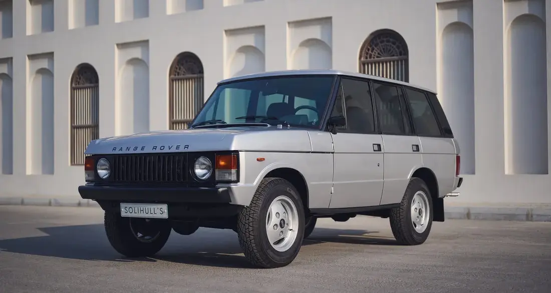 Range Rover Classic 1982 Silver Birch viertürig, aufgenommen im Originalzustand, seitlich frontal vor heller Gebäudefassade.