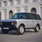 Range Rover Classic 1982 Silver Birch viertürig, aufgenommen im Originalzustand, seitlich frontal vor heller Gebäudefassade.