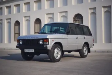 Range Rover Classic 1982 Silver Birch viertürig, aufgenommen im Originalzustand, seitlich frontal vor heller Gebäudefassade.