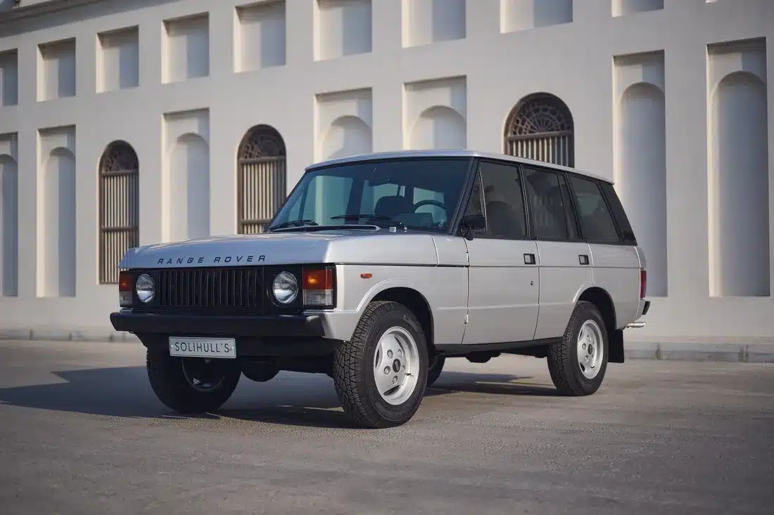 Range Rover Classic 1982 Silver Birch viertürig, aufgenommen im Originalzustand, seitlich frontal vor heller Gebäudefassade.