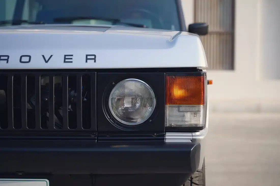 Frontpartie eines Range Rover Classic von 1982 in der Farbe Silver Birch mit Markenschriftzug, rundem Hauptscheinwerfer und orangem Blinker.