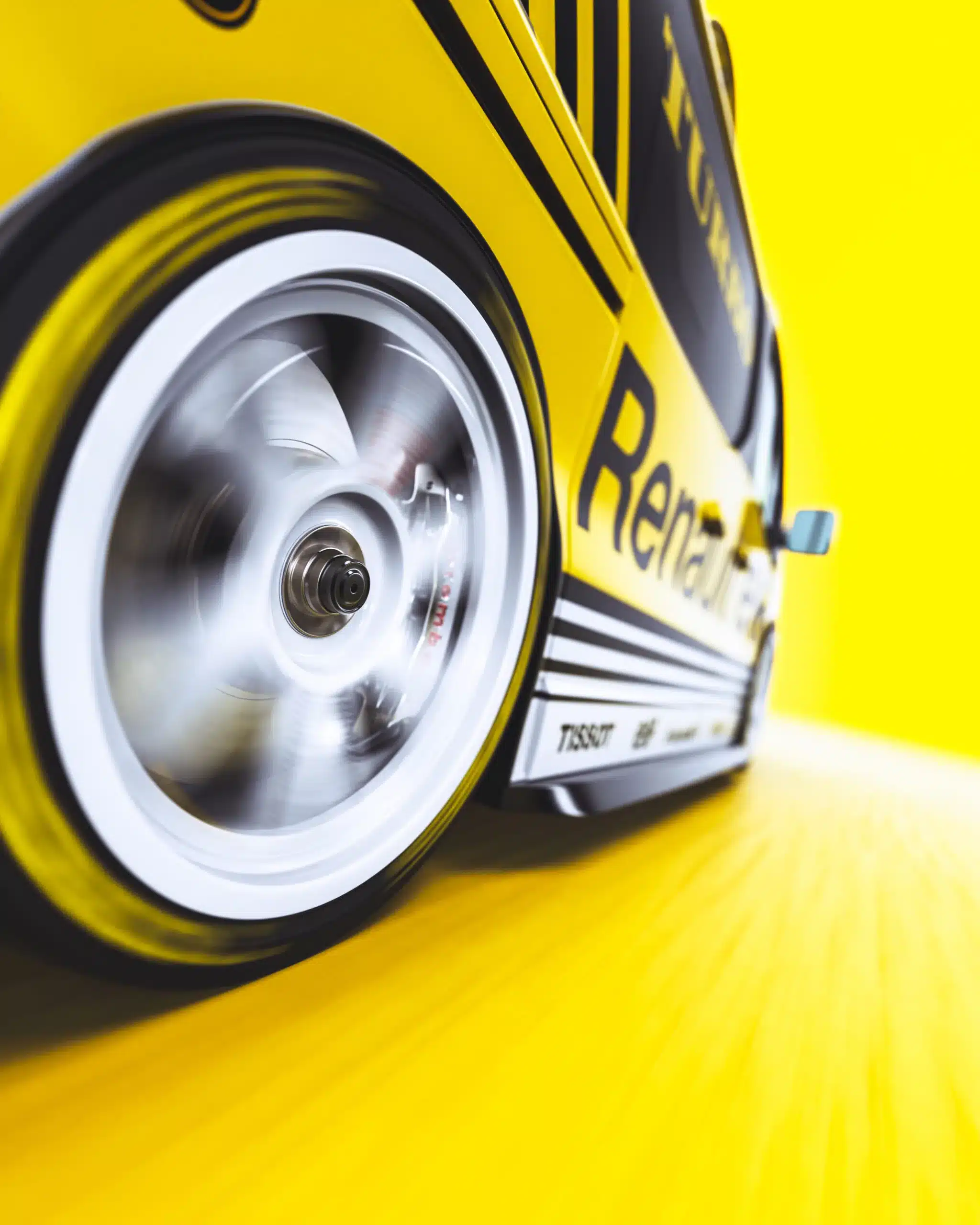 Nahaufnahme eines gelb-schwarz folierten Renault Trafic, Schwerpunkt auf dem rotierenden Rad vor gelbem Hintergrund.