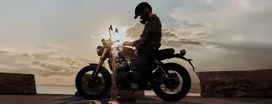 Fahrer auf einer Royal Enfield Bear 650 vor Sonnenuntergang an einer Küstenstraße