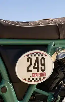 Seitliche Aufnahme der Royal Enfield Bear 650 mit Startnummerntafel 249, Scrambler-Sitzbank und Rahmen im Retro-Stil.