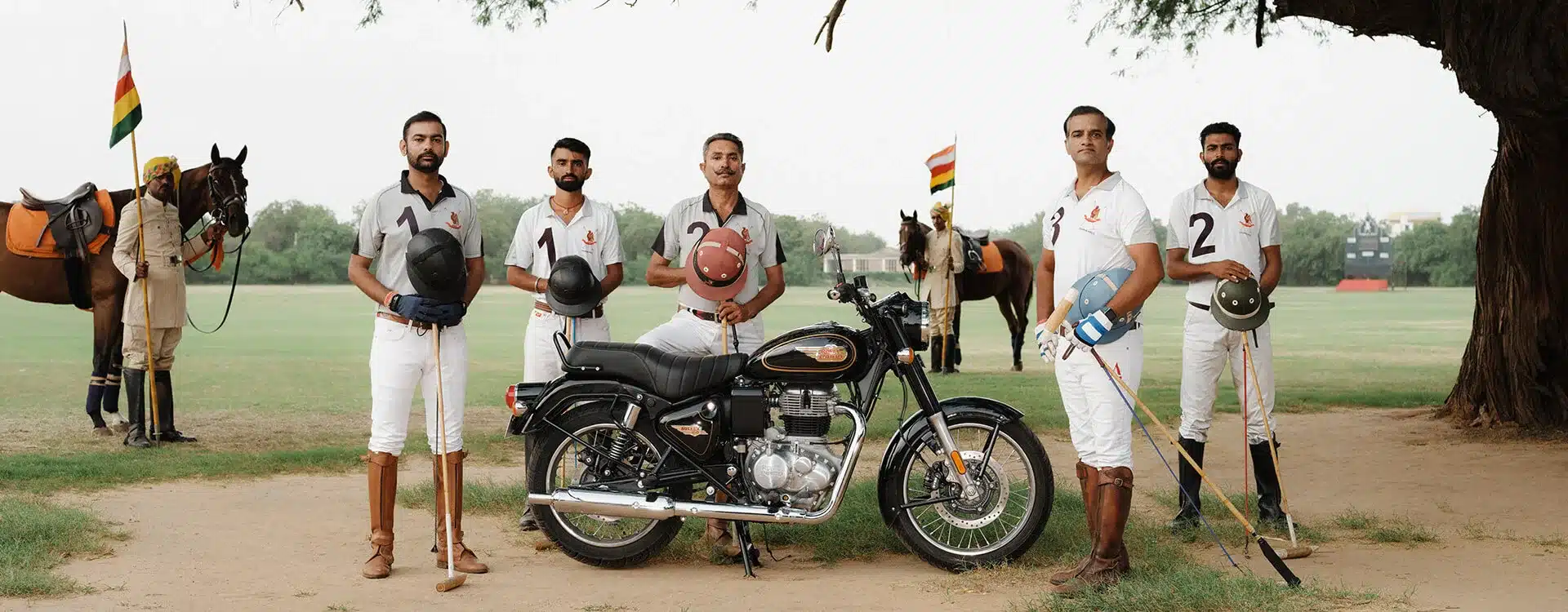 Royal Enfield Bullet 350 in Schwarz, eingerahmt von Polo-Spielern und Pferden, auf einem Sportplatz.