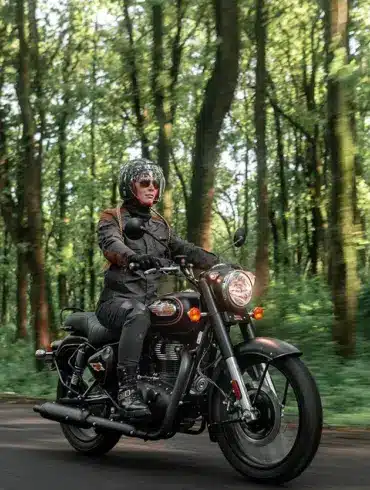 Motorradfahrer auf einer Royal Enfield Bullet 350 im Wald, modernes Modell in Schwarz.