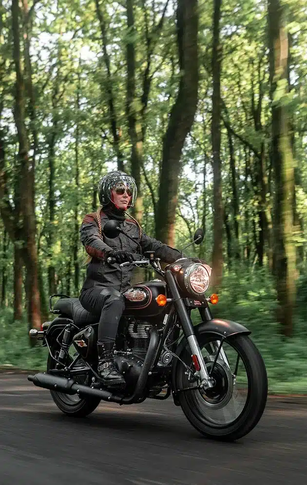 Motorradfahrer auf einer Royal Enfield Bullet 350 im Wald, modernes Modell in Schwarz.